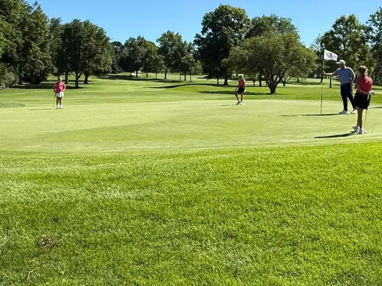 Juniors and a coach on the practice green during a junior golf clinic