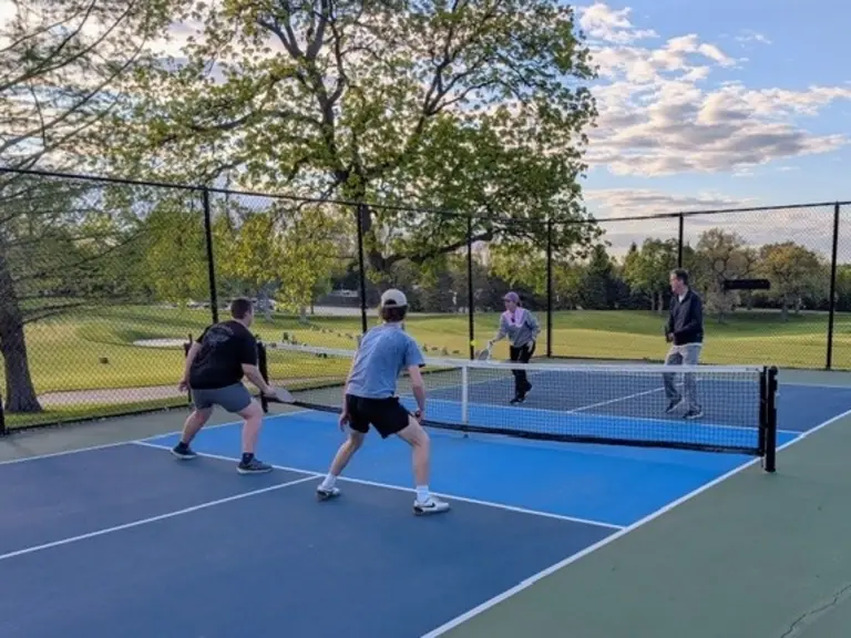 Four members mid-rally on the pickleball courts at golden hour
